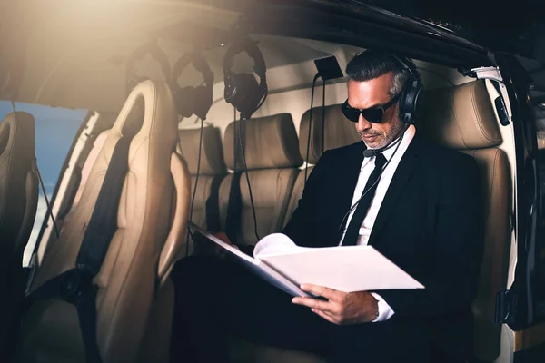 Putting those business plans in motion. a mature businessman reading through paperwork while traveling in a helicopter