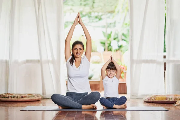 All together now. Portrait of a focused young mother and daughter doing a yoga pose together with their arms raised above their heads