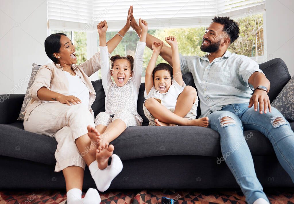 Happy parents and excited children celebrate on the sofa while watching tv. Fun family time, relaxing at home and bonding. Mother and father high five, kids cheer for sports team win