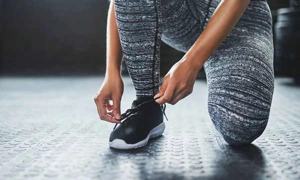 Good health starts now. a woman tying her shoelaces in a gym