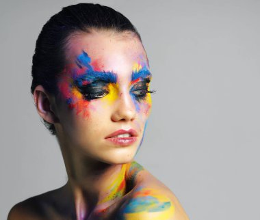Blue, yellow, red, repeat. Studio shot of an attractive young woman with brightly colored makeup against a gray background