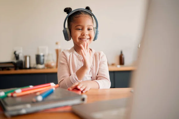 Distance learning, education and virtual student child on a video call lesson with a headset and laptop doing hello or bye greeting gesture. Little girl in an online classroom, homeschooling at home.