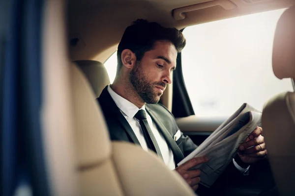 Reading newspaper early in the morning. a confident young businessman reading the newspaper while being seated in the backseat of a car