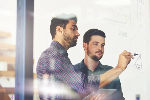 Planning together makes planning better. two young businessmen using a digital tablet while brainstorming on a glass wall in an office