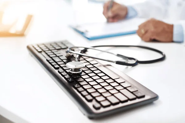 New school meets old school. a keyboard with a stethoscope on it while an unrecognizable man writes on a form in the background