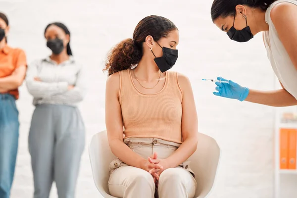 A covid vaccine of a young woman getting vaccinated for work in the office. Young wearing a mask female getting an injection or treatment to prevent the spread of coronavirus at the workplace.