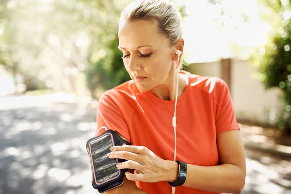 Mature, active and fit woman listening to music while running outside. Older person motivated for her positive, and athletic lifestyle. Female training for sport event or summer vacation body