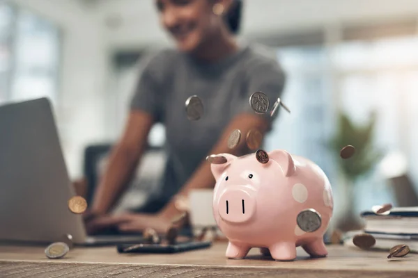 Financial strategy, investment or finance saving with a piggybank and coins falling out on a desk. Bank cash and money or digital budget growth of a person looking at online banking in the background.