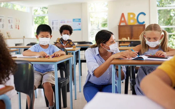 Covid learning with teacher and school students having lesson, study and education in class during pandemic. Educator helping, showing and talking to young kindergarten, preschool and elementary kids.