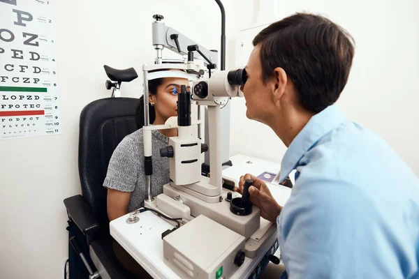 Eye and vision test, exam or screening with an optometrist, optician or ophthalmologist and a patient using an ophthalmoscope. Testing and checking eyesight for prescription glasses or contact lenses.