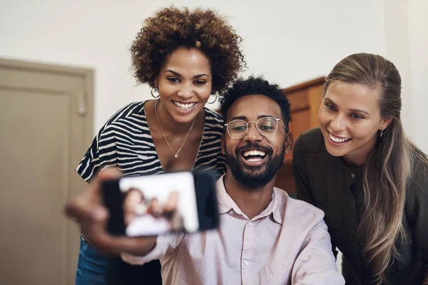 Diverse, fun and happy business people taking a selfie on a phone in an office together. Smiling group of colleagues and friends bonding, laughing and enjoying their positive, healthy friendship.