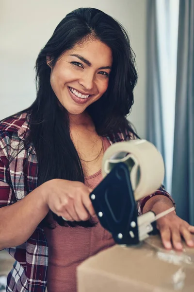 Packed and ready to make this move. Portrait of a young woman using tape to pack boxes while moving house