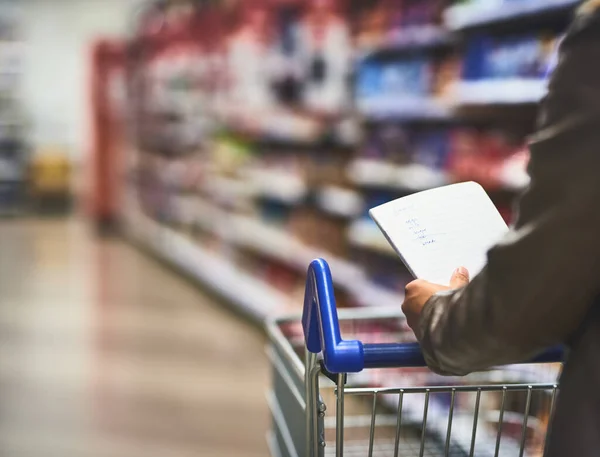Use a list and avoid over spending. a woman shopping with a list in a grocery store