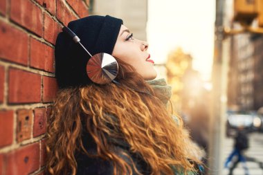 Music is my escape. a young woman listening to music while leaning against a brick wall outside