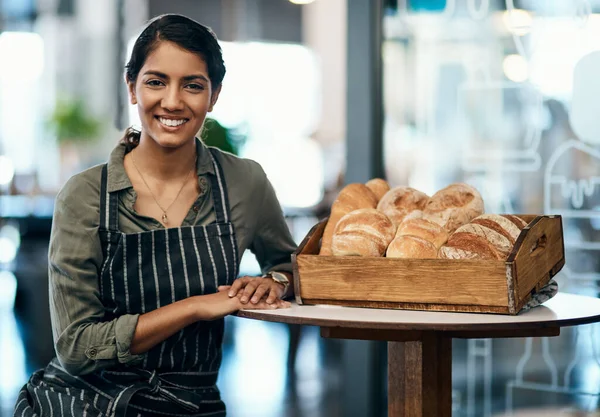 Portrait of a female restaurant waiter, baker or coffee shop retail manager with fresh bread for breakfast. Smiling, happy and young woman bakery worker ready to welcome a customer and work in a cafe.