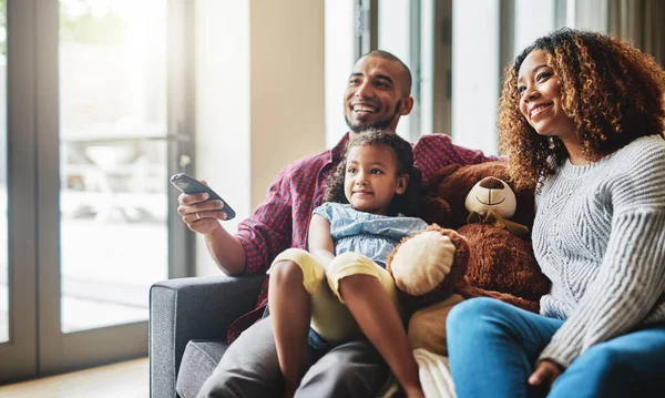 Looks like your favourite show is on sweetie. a happy young family of three watching tv together in their living room at home