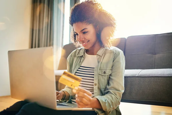 This is way better than standing in a queue. a cheerful young woman doing online shopping on her laptop while being seated on the floor at home