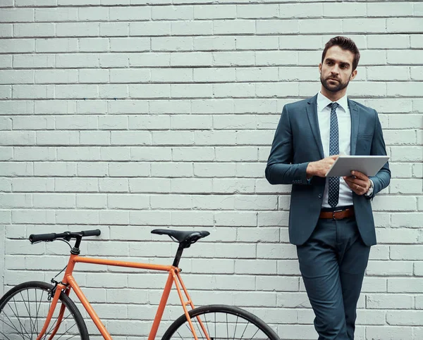 Everything he does is with convenience in mind. a handsome young businessman using a digital tablet while standing alongside his bike outdoors