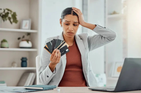 Financial stress, concerned and frustrated woman holding bank cards in her hand at her desk. Business female worried about economic decisions, credit interest or loan and debt in money crisis