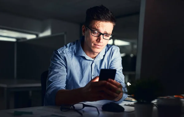 Confused businessman texting on his phone at the office at night. Handsome, confident and corporate caucasian male looking at messages from coworkers while working overtime and feeling unsure.