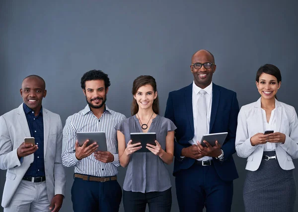 Using devices to its full potential to market the business. Studio shot of a group of corporate businesspeople using different devices against a gray background