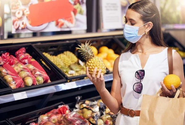 Woman grocery shopping while wearing a mask for medical protection against covid in a supermarket. Young female buying healthy, organic and wellness fruit consumables at a food store