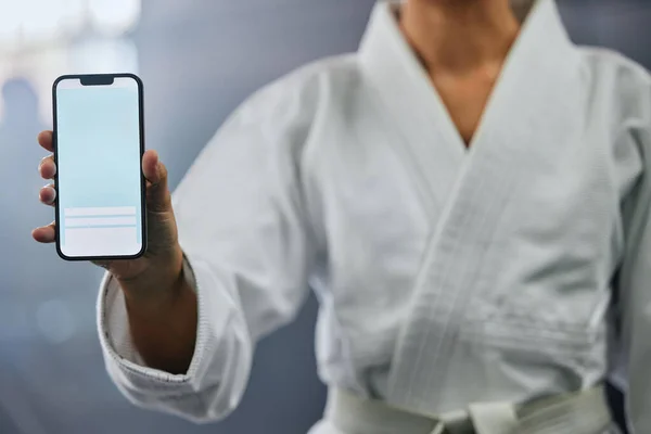 . Blank phone screen and copyspace with a karate student holding the mobile display indoors. Sport person showing a copy space announcing a sale, marketing or social media advertising content