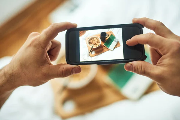 Food for thought and food for my tummy. High angle shot of an unrecognizable man taking a picture of his breakfast in bed at home