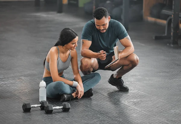 Personal trainer, coach or fitness instructor helping an active and fit woman in the gym. Young female athlete sitting down and managing her workout routine or schedule with her exercising partner.