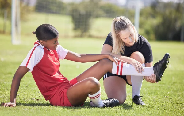Soccer, sports and injury of a female player suffering with sore leg, foot or ankle on the field. Painful, hurt and discomfort woman getting her pain checked out by athletic trainer on the pitch