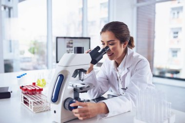 She stumbles across new findings everyday. a cheerful young female scientist looking through the lens of a microscope while being seated inside of a laboratory