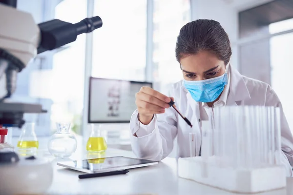 Cant afford to make mistakes. a focused young female scientist wearing a surgical mask and doing an experiment while being seated inside a laboratory