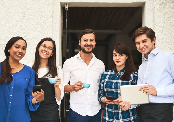 Meeting outside of the office. Portrait of a cheerful creative business team having a meeting and drinking coffee while looking at the camera outside