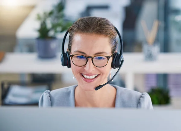 Call center agent helping clients online while talking on a headset in a modern office, enjoying her career. Customer service and support with a happy, friendly woman excited to guide and answer.