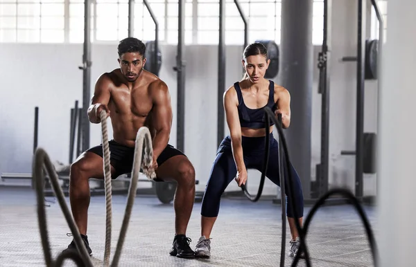 Active, fitness partners training together, exercising with battle ropes in gym. Athletic sports couple in motion doing arms and cardio workout in wellness center for strength and healthy lifestyle