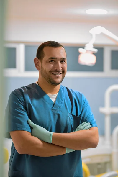 He will see to it that you have a bright smile everyday. Portrait of a cheerful young male dentist standing with his arms folded while looking at the camera in his office