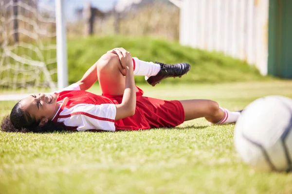 Injured, pain or injury of a female soccer player lying on a field holding her knee during a match. Hurt woman footballer with a painful leg on the ground in agony having a bad day on the pitch.