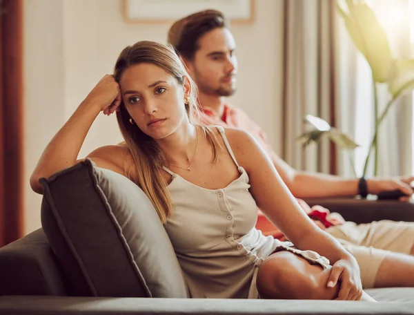 Unhappy, sad and annoyed couple after a fight and are angry at each other while sitting on a couch at home. A woman is stressed, upset and frustrated by her boyfriend after an argument.