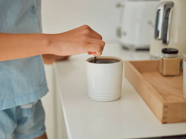 Making fresh, hot morning coffee indoors on a kitchen counter to start the day. Hand closeup of preparing a warm beverage and drink inside with a female standing in pajamas at home.