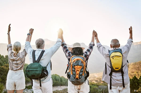 Hiking group, celebration and success on mountain peak after climbing and walking up remote hills. Cheering, motivated or proud mature friends with arms up on adventure in remote eco nature landscape.