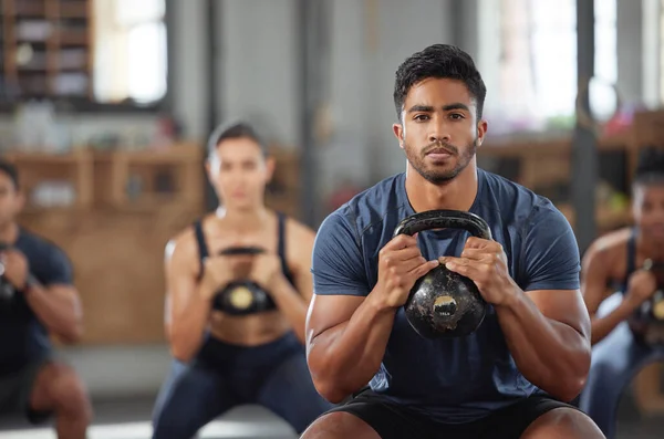 Personal trainer squatting with a team of athletes in a workout session at a fitness club. Portrait of a fit, active and serious young male coach using a kettlebell and training a group of people.