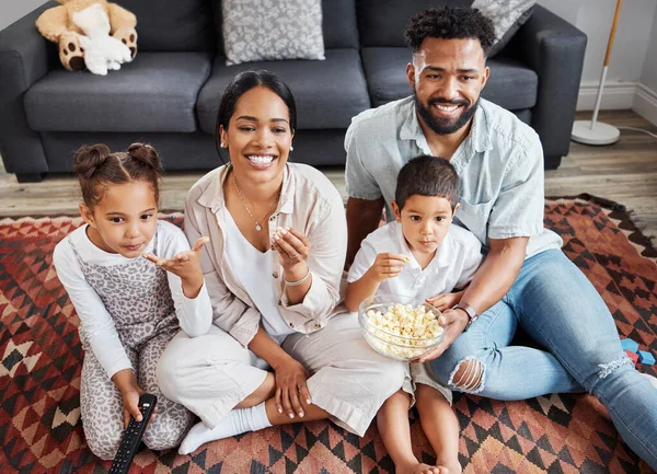 Watching movie, family bonding and eating popcorn while relaxing in the lounge together at home. Happy, smiling and carefree parents enjoying snack, looking at comedy series, laughing with kids.