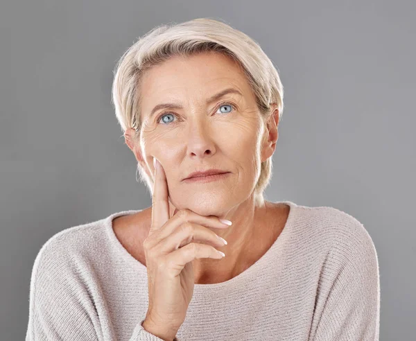 Mature, thinking and woman touching her face in isolated grey studio background. Copy space for anti ageing skincare or cosmetic products for senior feeling her skin and wrinkles headshot