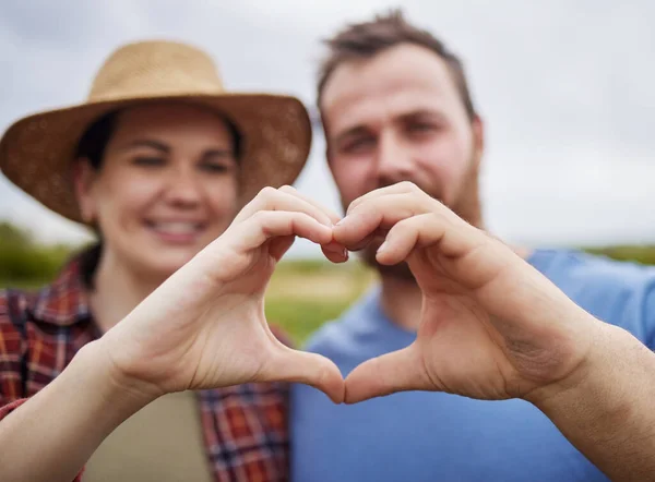 Farmer couple support sustainability by making a love heart sign with their hands outdoors on an organic farm. Happy and carefree activists with a passion for sustainable and organic farming.