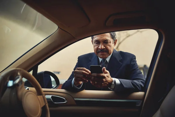 Pulling over to reply to an email. a mature businessman using a phone while leaning against his car