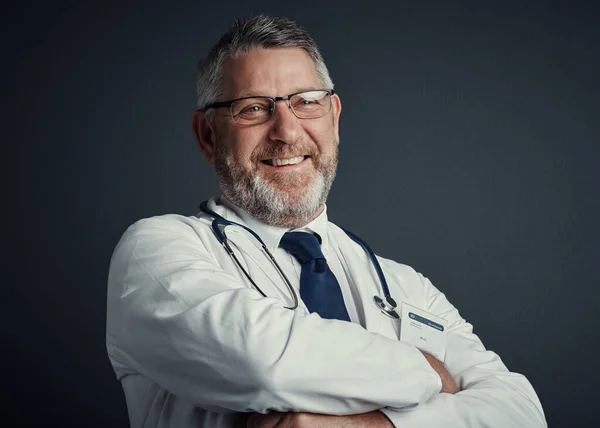 Im happy to help. Studio portrait of a handsome mature male doctor standing with his arms folded against a dark background