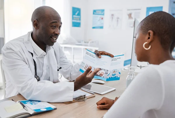 A doctor giving patient hospital information at a clinic and explaining medical benefits to a woman in his office. African American GP or healthcare professional having a discussion with a female.