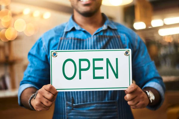 Open for business. Closeup shot of an unrecognizable man holding up an open sign in his store