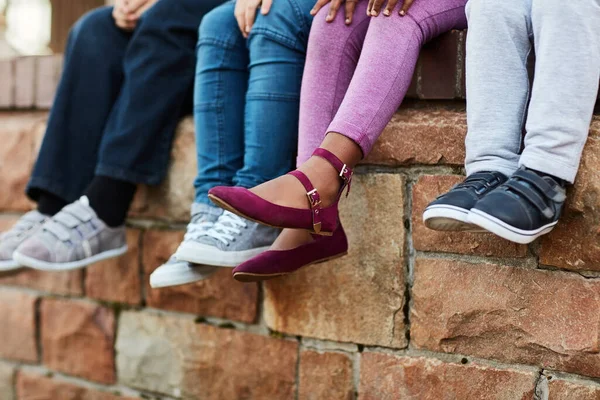 New shoes for the new school year. unrecognizable elementary school kids sitting on a brick wall outside