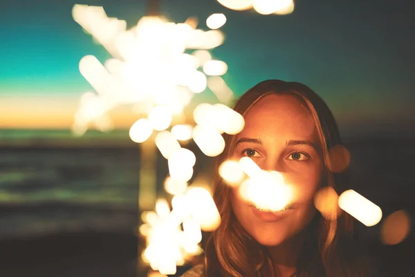 Light up your life. a young woman holding a sparkler at the beach at night